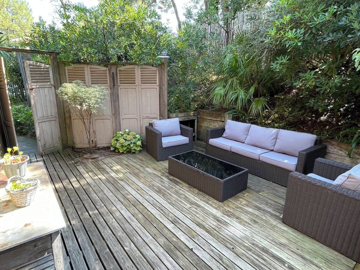 An outdoor patio with a wooden deck, wicker furniture, and a covered area with a wooden door.