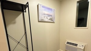 Una habitación con una estantería de metal negro, un cuadro enmarcado de una playa, una ventana y un aire acondicionado instalado en la pared.