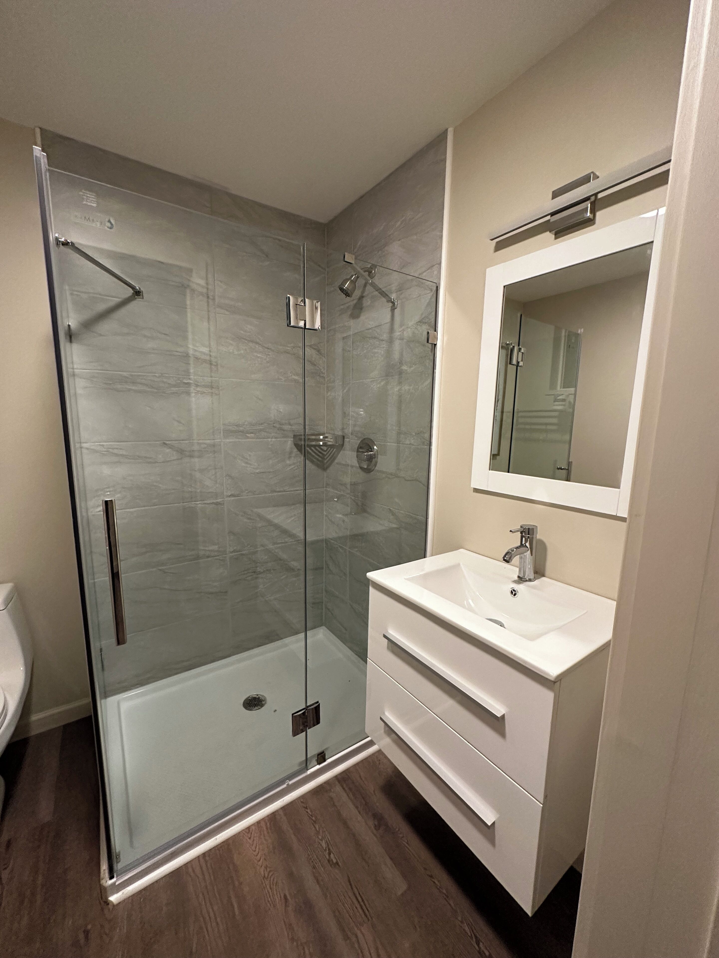 A modern bathroom with a glass-enclosed shower, a white vanity with a sink, and a mirror above the vanity.