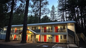 Un motel de estructura de dos pisos, con varias puertas rojas y un área de estacionamiento señalizada con 'No Estacionar'.