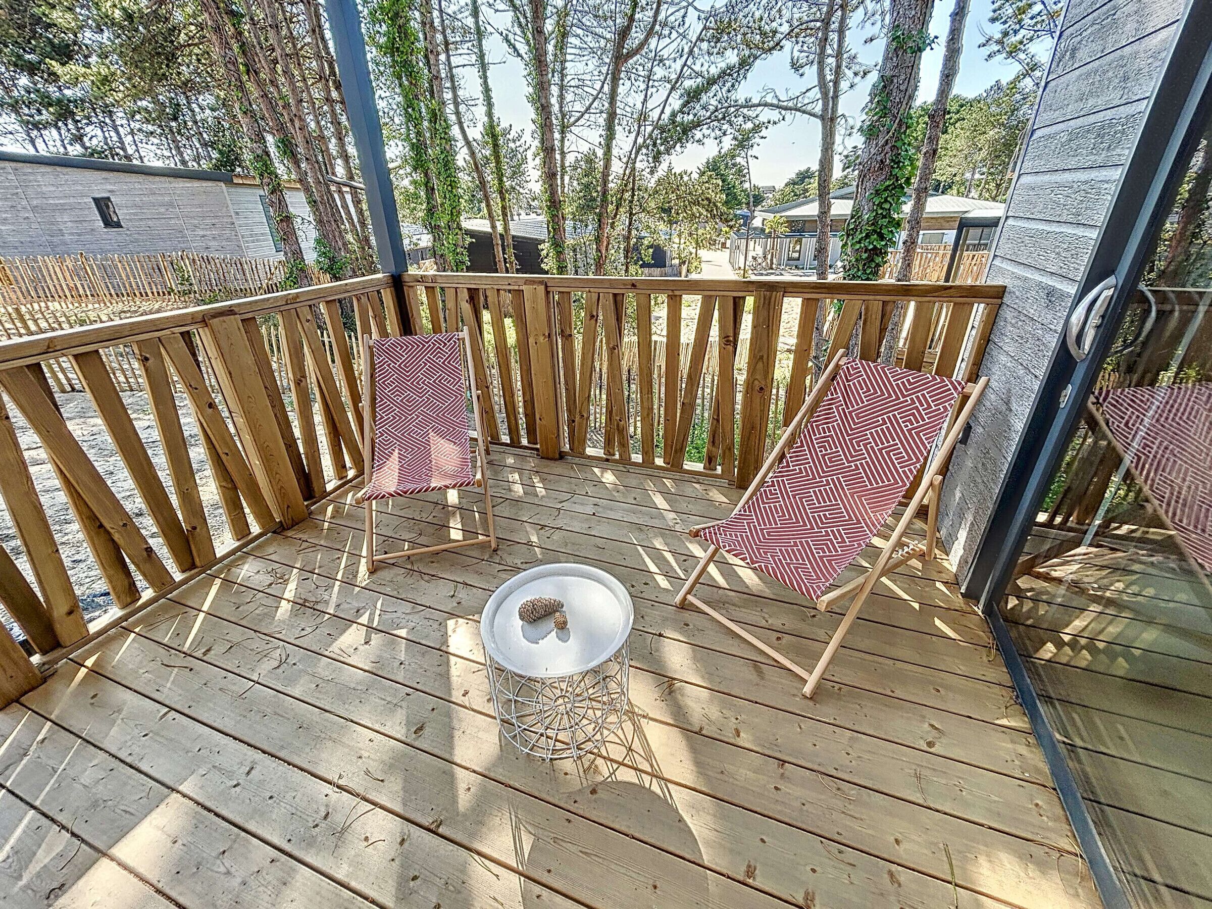 Une terrasse en bois avec deux chaises à motifs et une petite table, le tout entouré d’une clôture en bois.