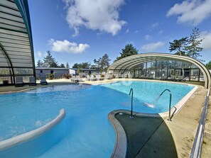A swimming pool with a curved edge, surrounded by lounge chairs and a covered area with large windows.