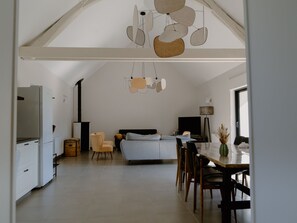 A spacious living area with a high ceiling, a bed, a dining table, and a kitchen area.
