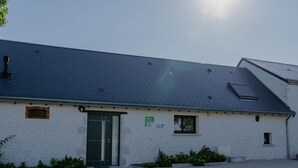 A white building with a dark roof, a green door, and a small window. There is a sign on the wall and a garden area in front.