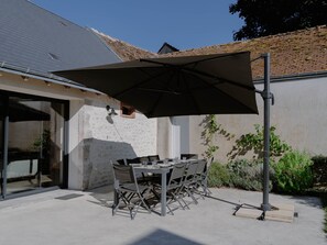 Une terrasse extérieure avec une table et des chaises, un grand parasol et un mur en pierre.