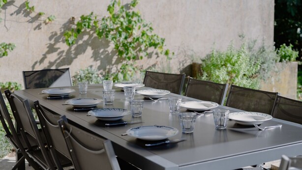 A table set outdoors with plates, glasses, and chairs.