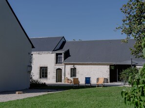 Un bâtiment à deux étages, doté d’un toit en pente, d’un petit jardin avec une pelouse et de trois chaises d’extérieur.