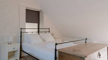 A bedroom with a sloped ceiling, a bed with white bedding, a wooden dresser, and a nightstand with a lamp.