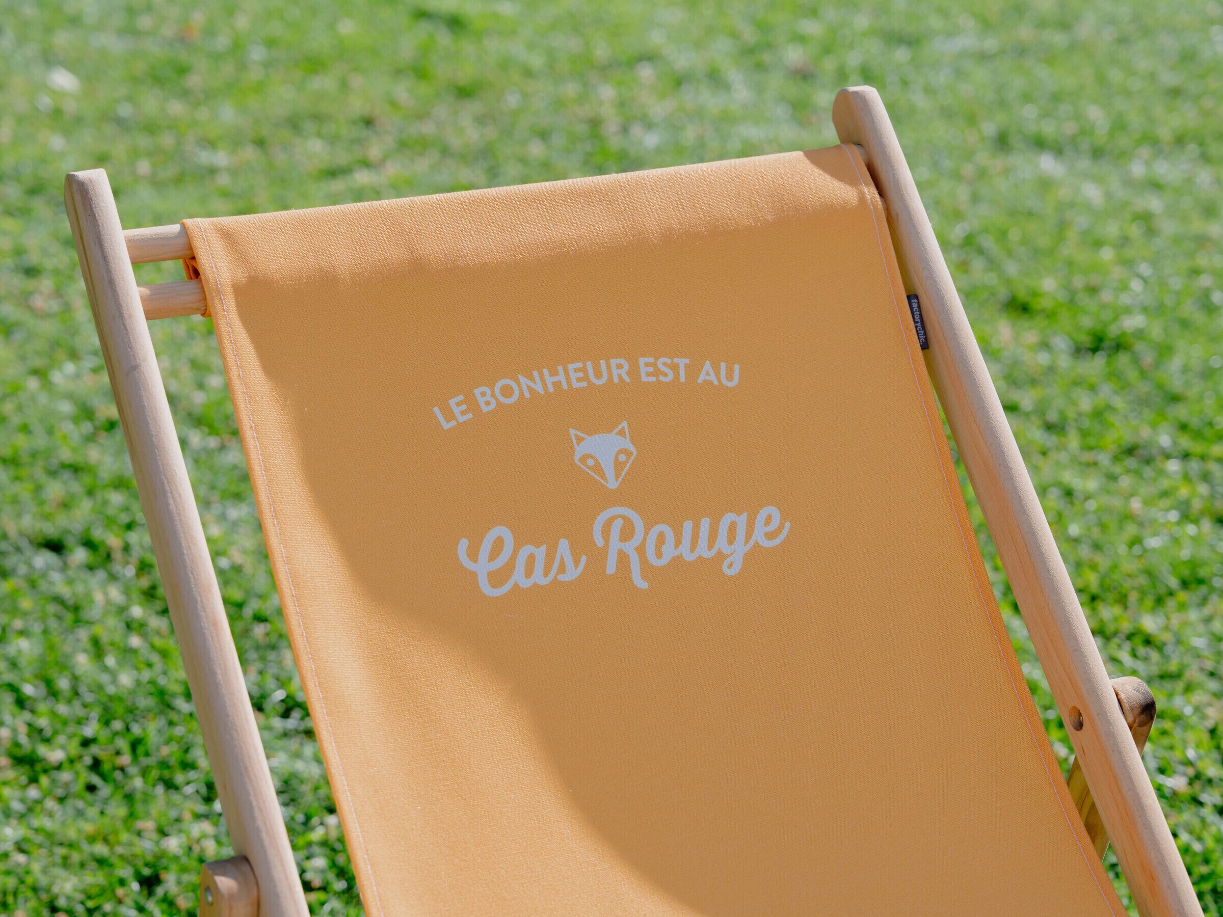 A wooden chair with a yellow fabric backrest and a logo that reads "Le Bonheur est au Cas Rouge".