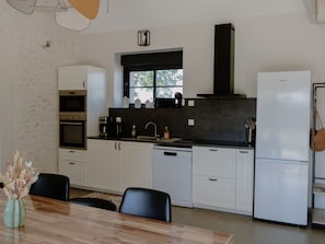 A modern kitchen with white cabinets, a black countertop, a built-in oven, a dishwasher, and a refrigerator.
