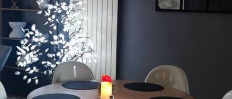 A dining area with a round table, white chairs, a decorative white tree, and a lit candle.