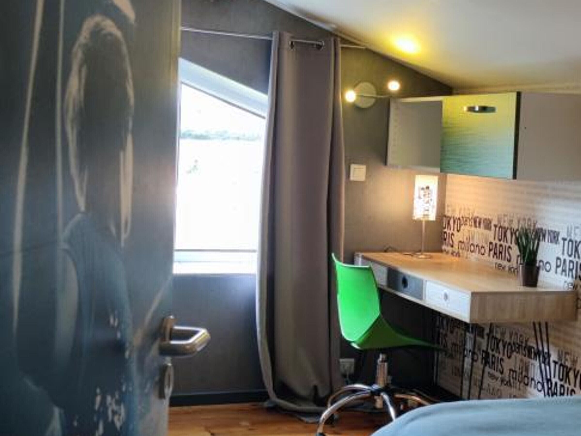 Ein modernes Hotelzimmer mit großem Fenster, einem grünen Sessel und einem Schreibtisch mit Lampe.