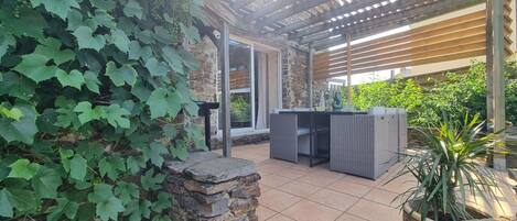 An outdoor patio area with a pergola, stone wall, and wicker furniture.