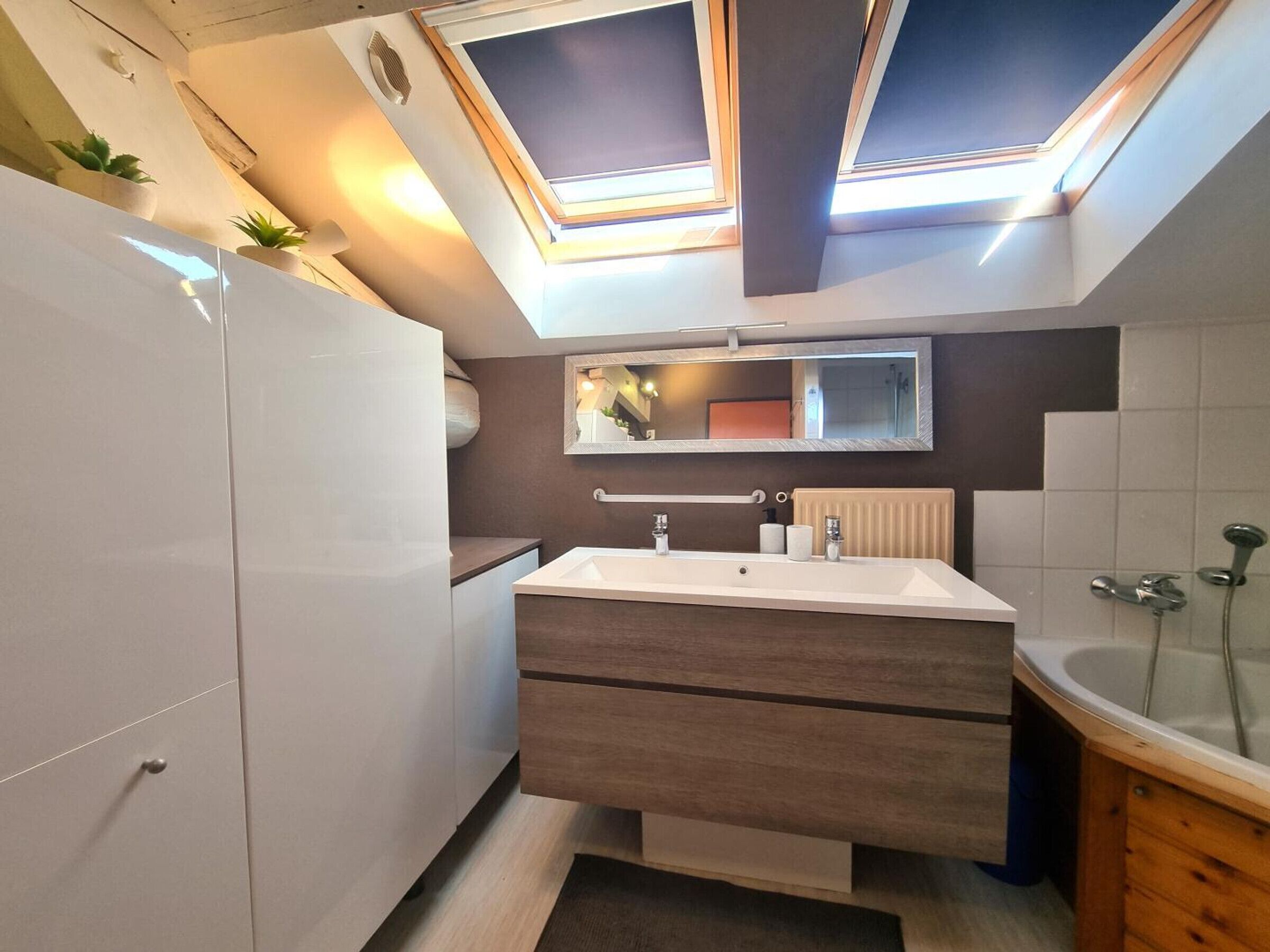 Un baño moderno con tragaluces, un espejo grande, una bañera independiente y un mueble de tocador de madera.