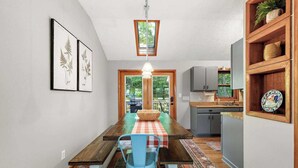 A dining area with a wooden table, blue chairs, and a checkered tablecloth. There is a kitchen area with cabinets and a window. - Front Porch Therapy - Escape to your hideaway only 6 minutes above Boone (Boone)
