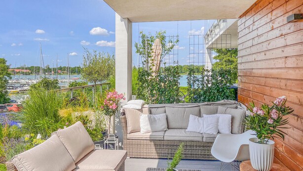 A balcony with a wicker sofa, white cushions, and a potted plant. - 2 bedroom beautiful apartment in Rydzewo (Rydzewo)