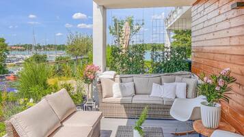 Un balcon avec un canapé en osier, des coussins blancs et une plante en pot.