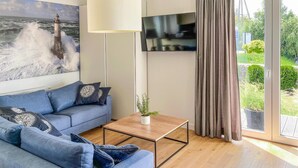 A modern living room with a blue sofa, a coffee table, a TV, and a large window with curtains. - 2 bedroom beautiful apartment in Rydzewo (Rydzewo)