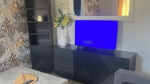 Una sala de estar con una televisión de pantalla plana, una mesa de centro, un sofá, una estantería y un jarrón decorativo con flores.