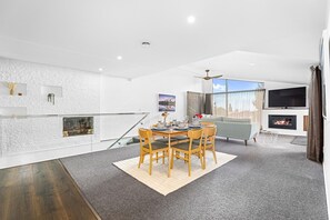 A modern living room with a dining area, a fireplace, and a large window with a view. - Redwoods Getaway - 100m to the Trails, Sleeps 7 (Rotorua)