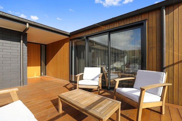 An outdoor deck with wooden furniture and a glass wall.