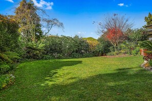 A well-maintained garden with a variety of plants and trees, a clear sky, and a grassy lawn. - Redwoods Getaway - 100m to the Trails, Sleeps 7 (Rotorua)