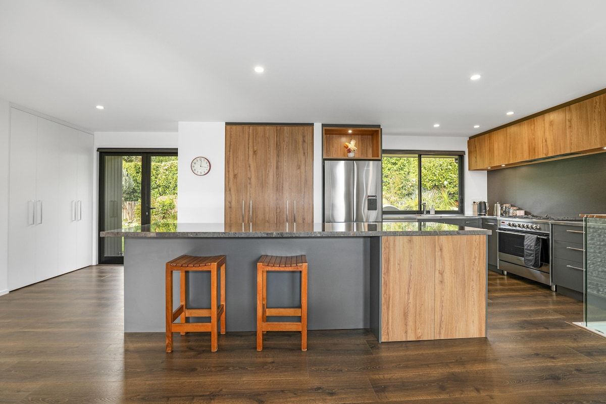 A modern kitchen with a central island, wooden cabinets, stainless steel appliances, and two wooden stools.