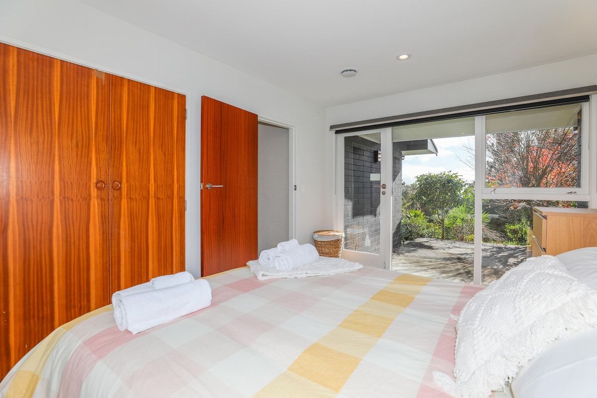 A bedroom with a large bed, a wooden wardrobe, and a sliding glass door leading to a balcony.