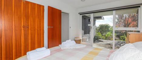 A bedroom with a large bed, a wooden wardrobe, and a sliding glass door leading to a balcony.