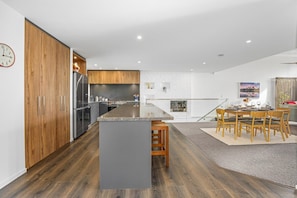 A modern kitchen with wooden cabinets, a central island, and a dining area with a table and chairs. - Redwoods Getaway - 100m to the Trails, Sleeps 7 (Rotorua)