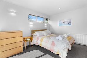 A bedroom with a bed, bedside table, wooden dresser, and a window with a view. - Redwoods Getaway - 100m to the Trails, Sleeps 7 (Rotorua)