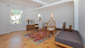 Um quarto amplo com uma janela grande, uma cadeira de madeira, um sofá e um tapete estampado.
