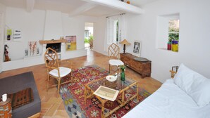 Uma sala de estar espaçosa com lareira, duas poltronas de vime, um sofá, uma mesa de centro de vidro e um tapete estampado.