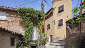 Uma rua estreita ladeada por edifícios, com paredes de pedra e venezianas de madeira nas janelas.