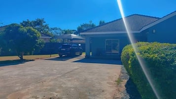 A residential driveway with a parked car, a house with a tiled roof, and a well-maintained hedge.