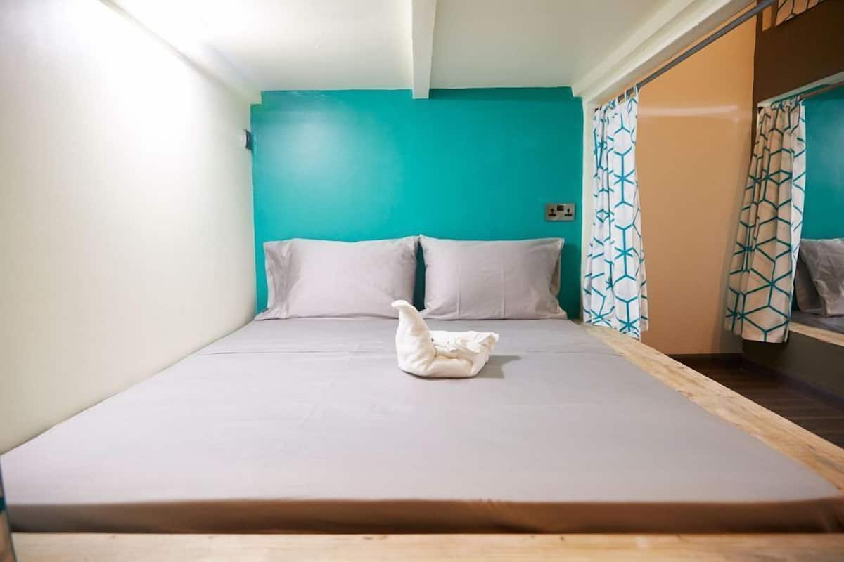 A single bed with a white mattress and pillows, a teal wall, and patterned curtains.