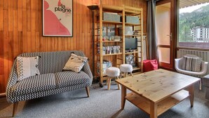 A cozy living room with a patterned sofa, a wooden coffee table, and a bookshelf filled with books and decorative items. - Large duplex for 8 people, south facing (La Plagne)