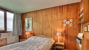 A bedroom with a wooden paneled wall, a bed with white bedding, a nightstand with a lamp, a dresser, and a bookshelf. - Large duplex for 8 people, south facing (La Plagne)