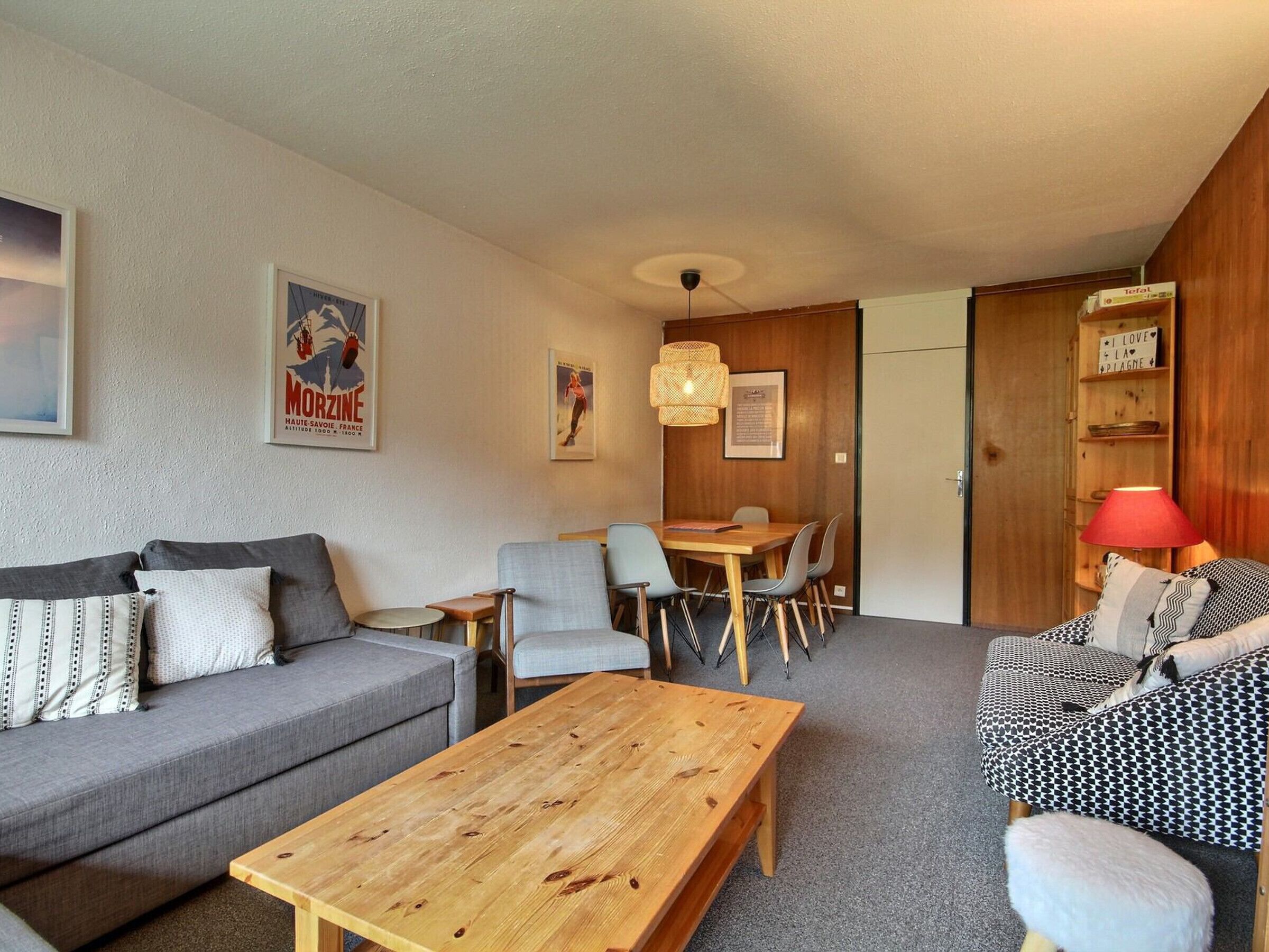 Un salon moderne avec un canapé gris, une table basse en bois et un coin repas comprenant des chaises et une table.