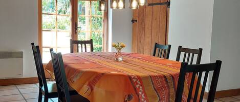 Un área de comedor con una mesa grande cubierta con un mantel estampado, rodeada de sillas, bajo un techo de madera con vigas a la vista.