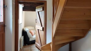 Una escalera de madera que conduce a un piso superior, una puerta blanca con un ventanal y un sofá beige en una habitación con suelo de baldosas.