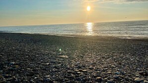Uma praia de seixos com o sol a pôr-se no horizonte.
