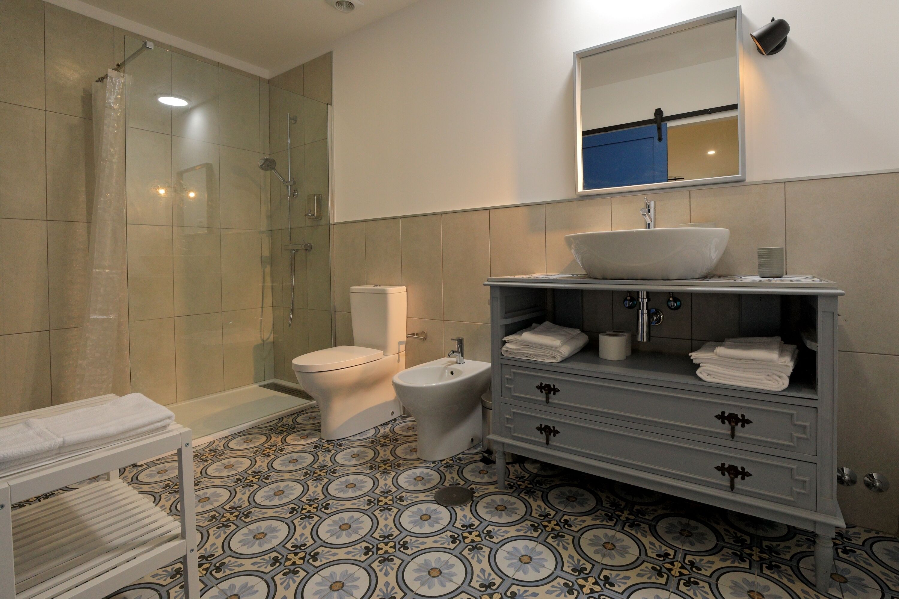 A bathroom with a shower, toilet, bidet, vanity with a sink, and a towel rack.
