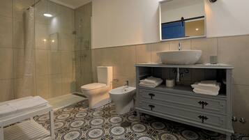 A bathroom with a shower, toilet, bidet, vanity with a sink, and a towel rack.
