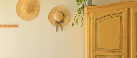 Une pièce avec un meuble en bois, deux chapeaux de paille accrochés au mur et une plante en pot.