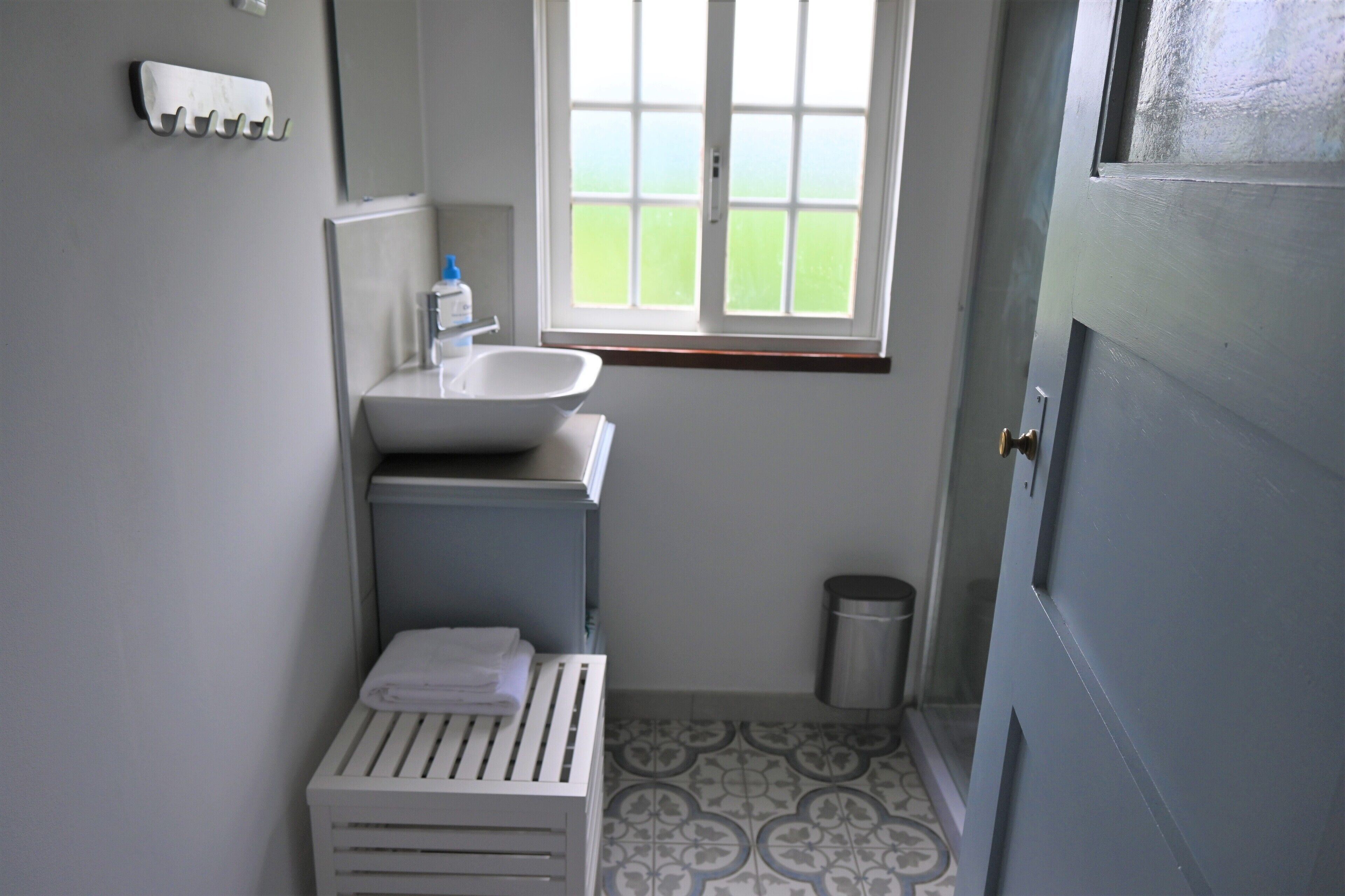 A small bathroom with a white sink, a toilet, a window, and a trash can.
