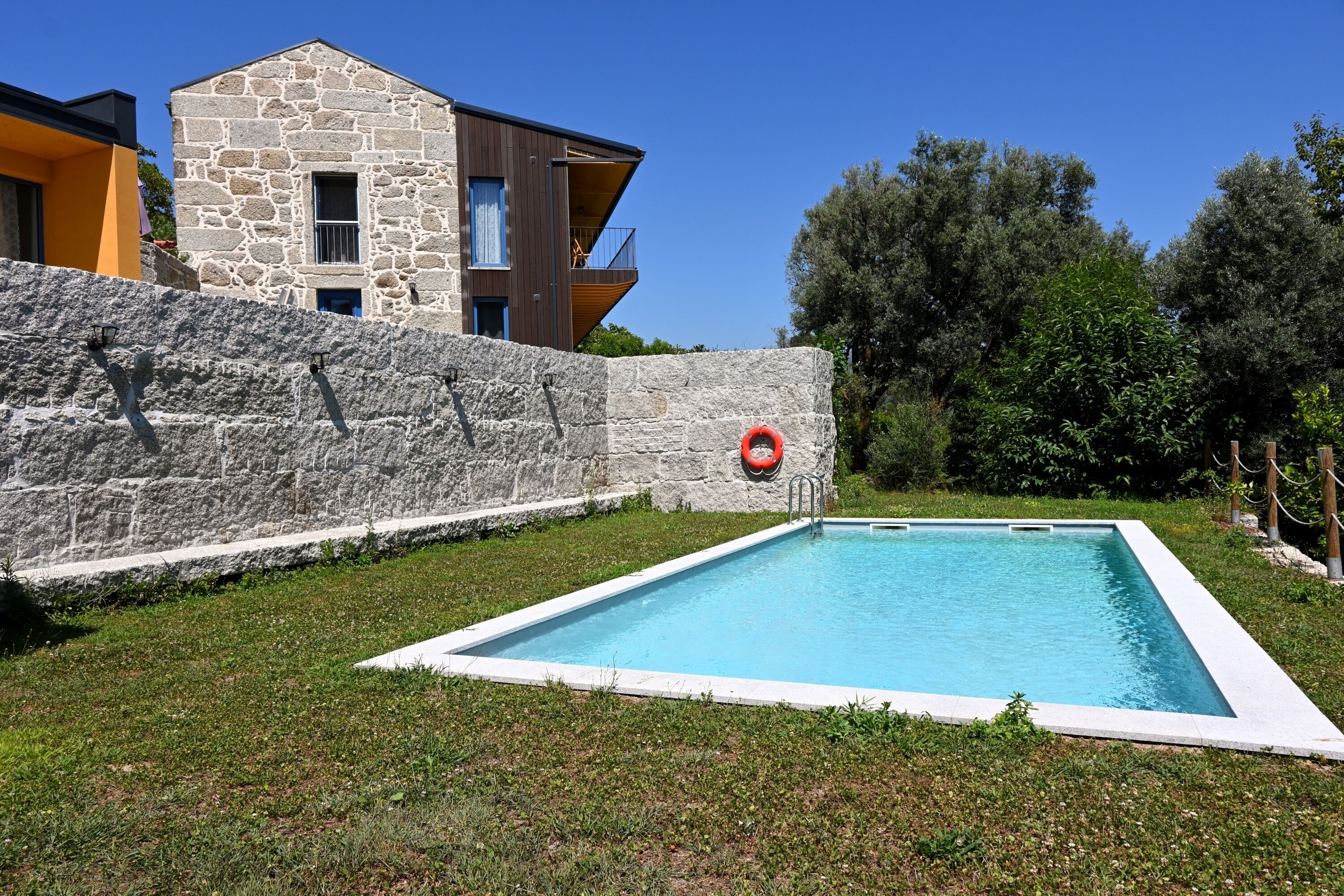 A swimming pool surrounded by a stone wall, with a modern building in the background.