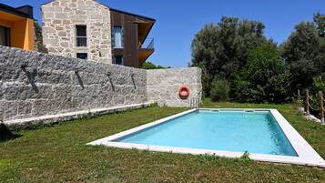 A swimming pool surrounded by a stone wall, with a modern building in the background.
