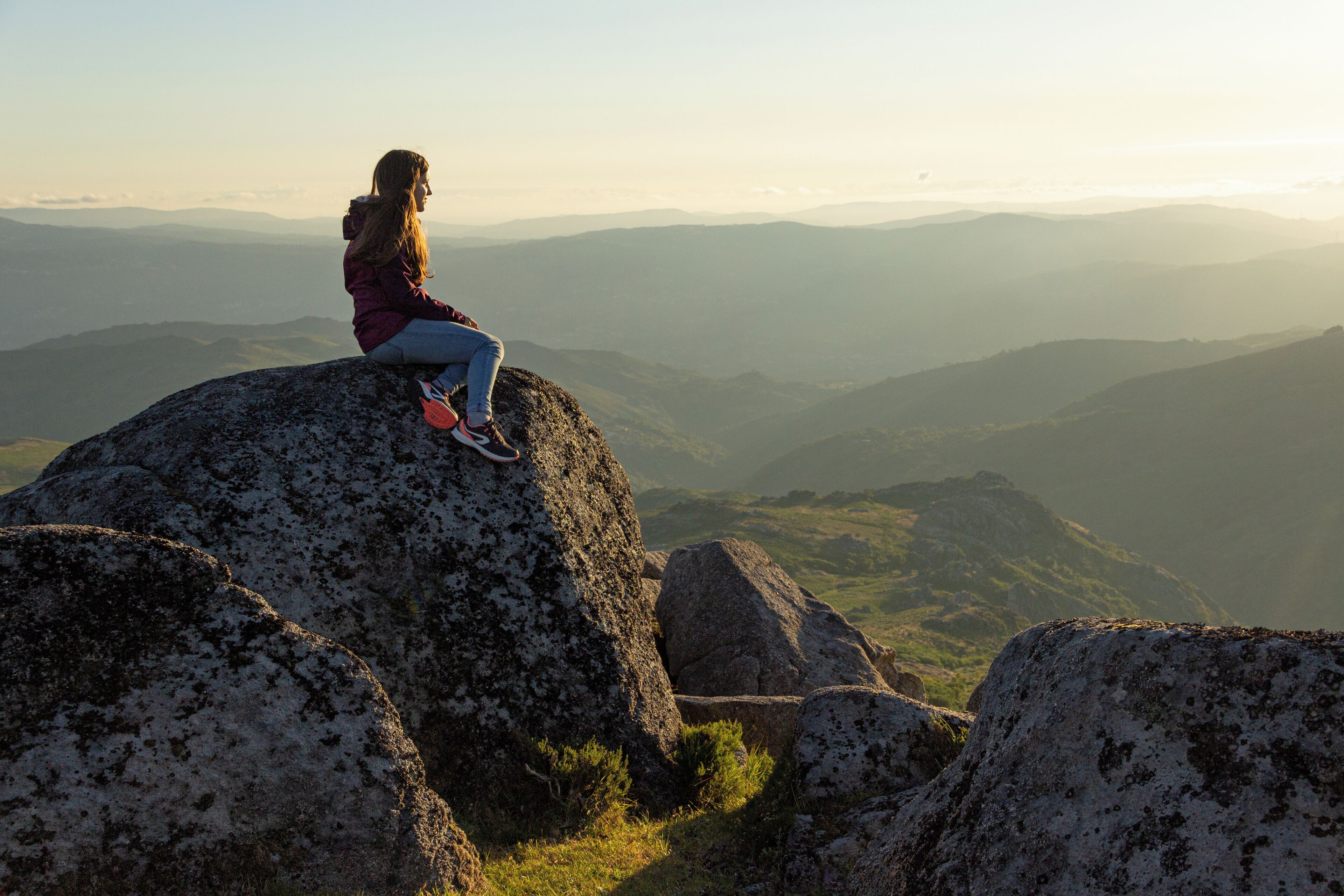 A person sitting on a rock with a view of a mountainous landscape.