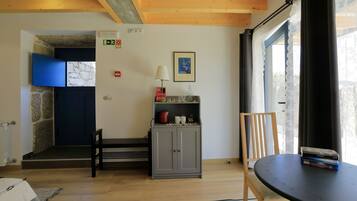 Una habitación con techo de madera, pared de piedra, puerta azul, armario gris, una mesa con libros y una silla.